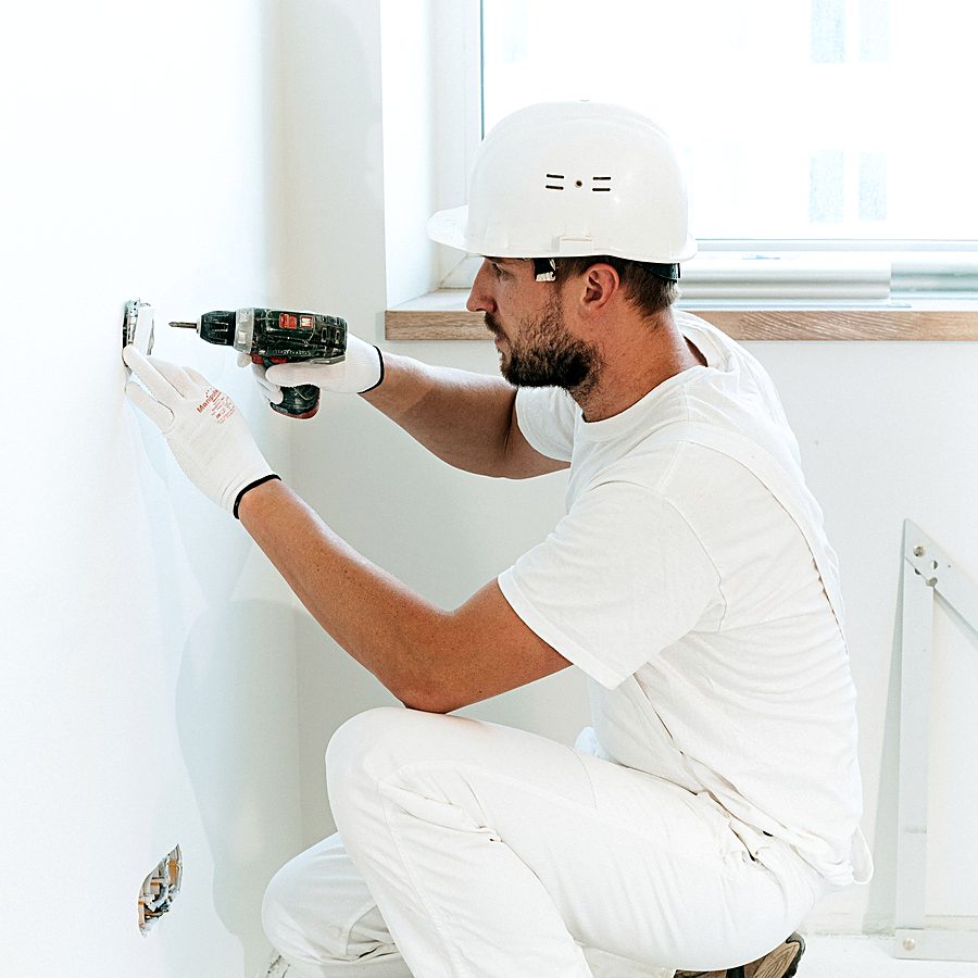 Electrician in a hard hat installing a wall fitting during a renovation