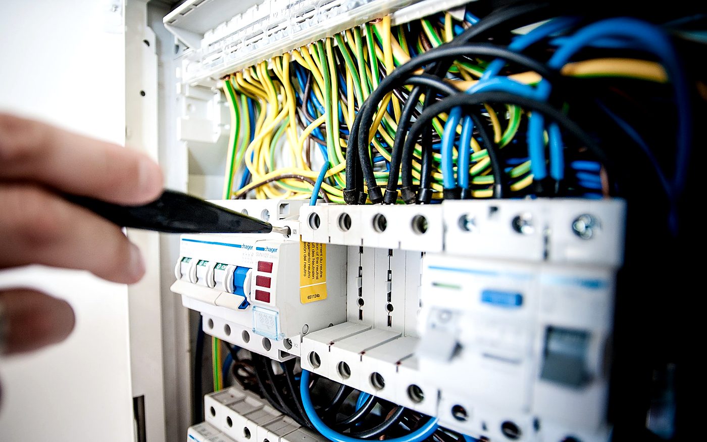 Electrician's hand using pliers on a switchboard full of colour-coded wiring