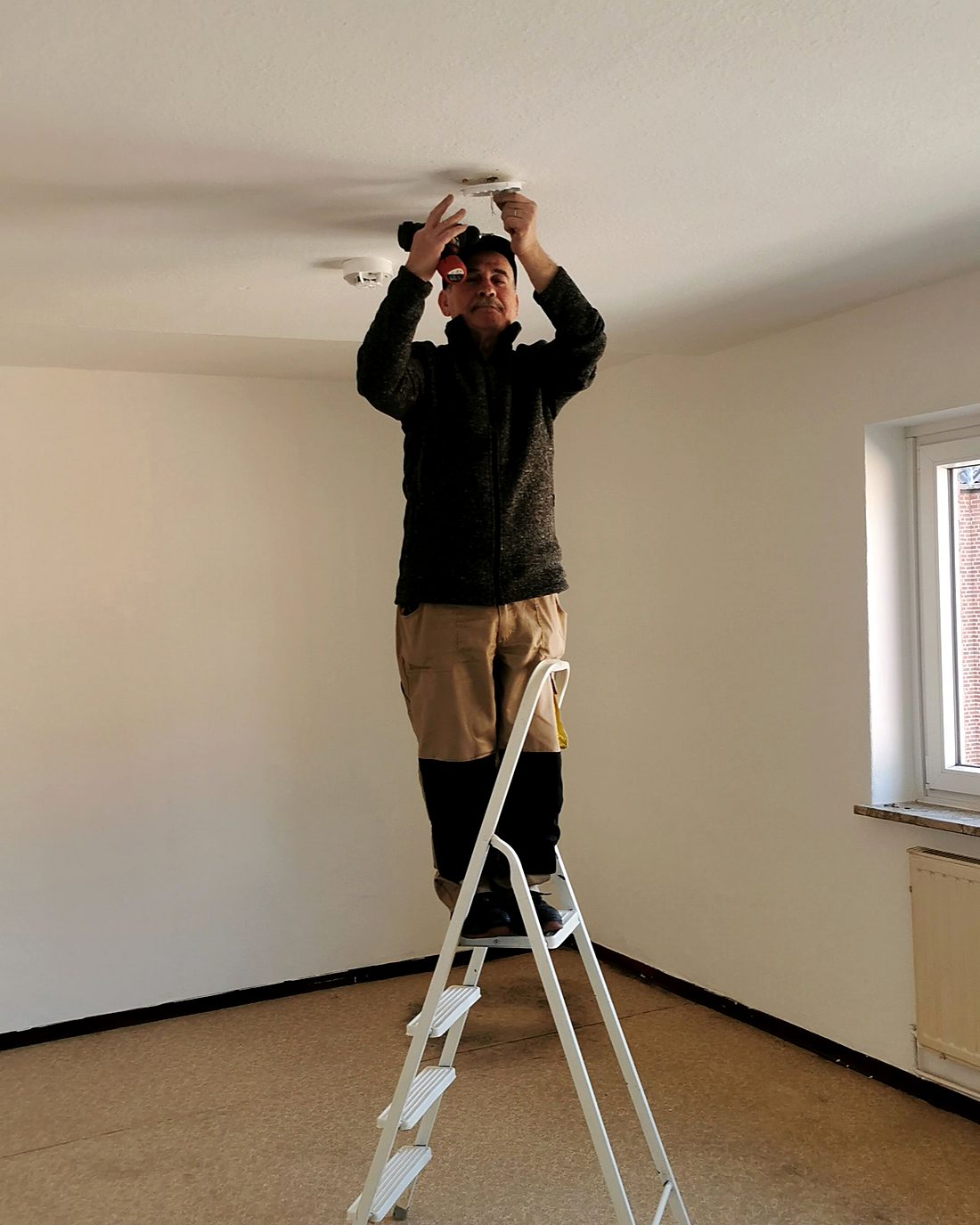 Electrician on a ladder installing a ceiling light fitting during a home renovation